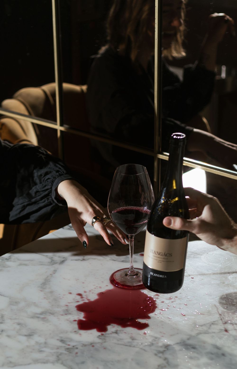 Wine spilled on marble countertop next to glass and bottle in moody lighting.