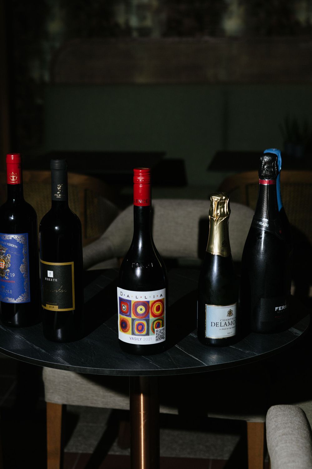 Collection of wine and champagne bottles arranged on dark round table in dim lighting.