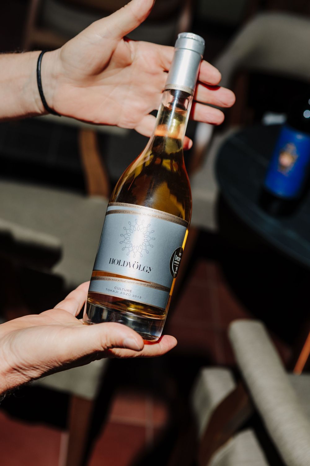 Hands passing a bottle of white wine with silver label between people.