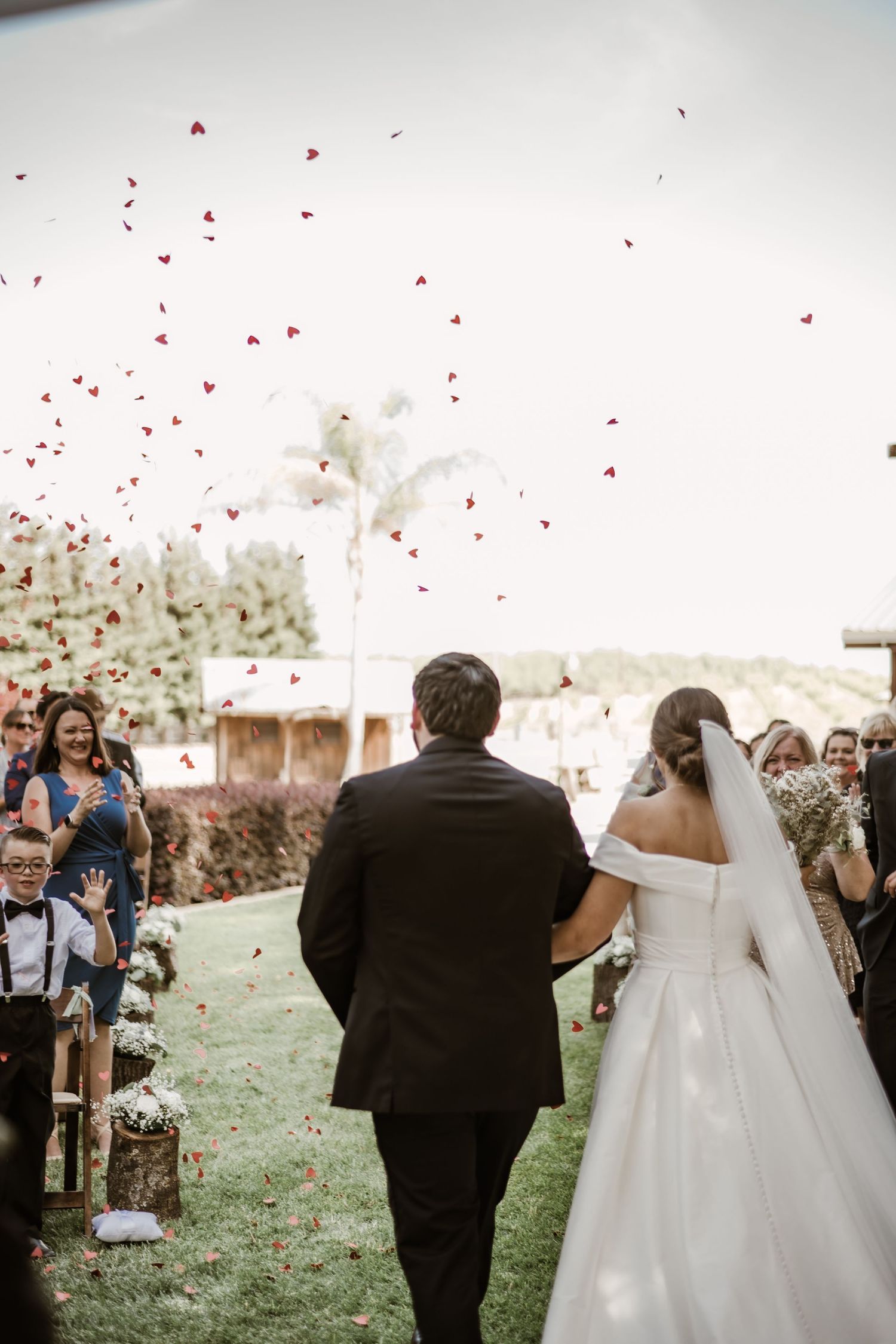 Wedding celebration with red rose petals being tossed in the air by guests.