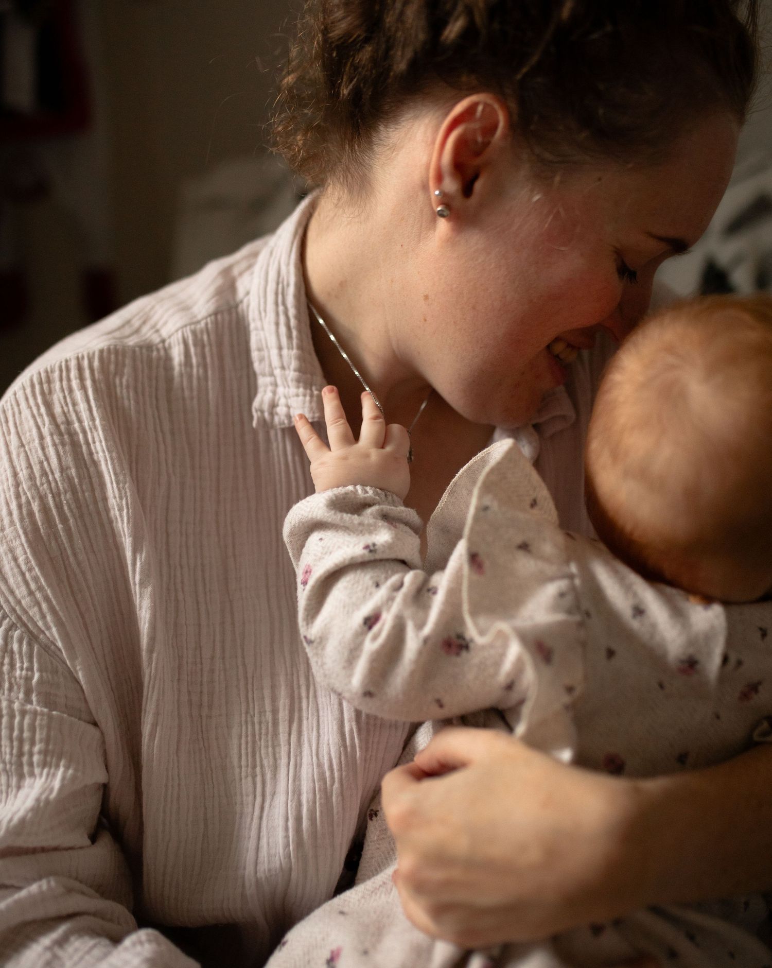A tender intimate moment is shared as someone holds and nuzzles close to their baby in natural lighting.