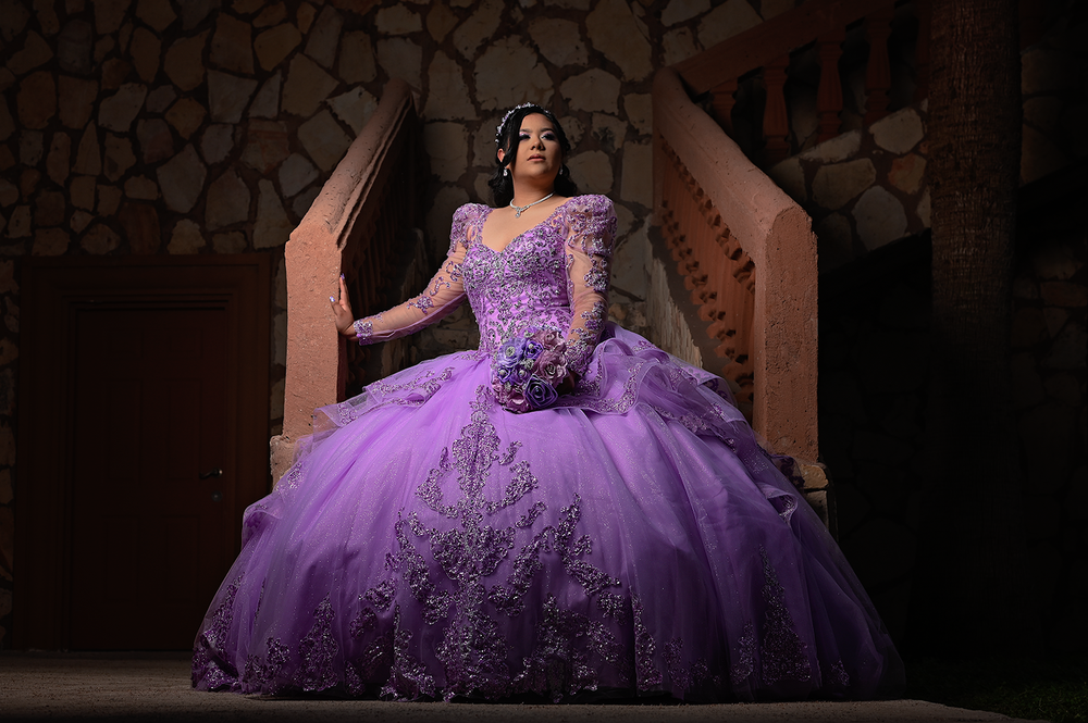 Dramatic evening portrait of a purple ball gown against rustic stone architecture.