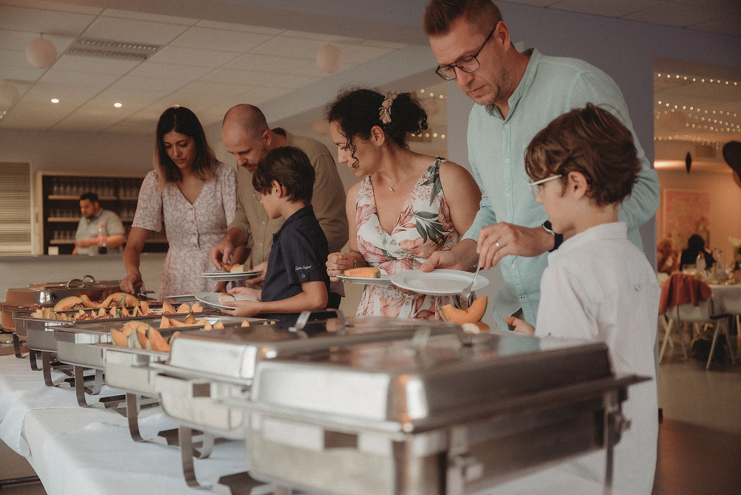 Guests serve themselves at a buffet line with chafing dishes at a wedding reception.