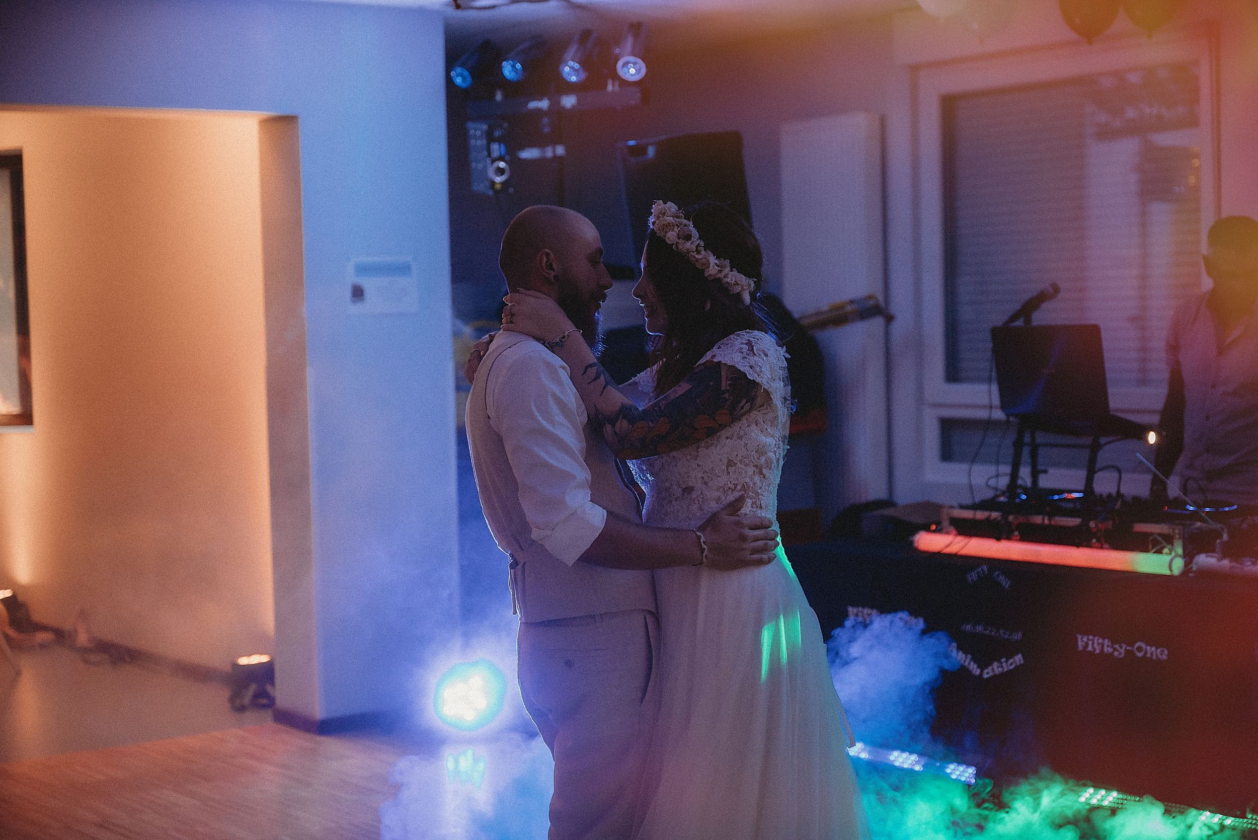 A couple shares their first dance in a dimly lit reception venue with blue lighting.