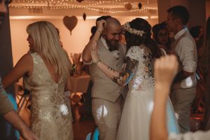 Wedding party dancing together under warm string lights and decorative hearts.