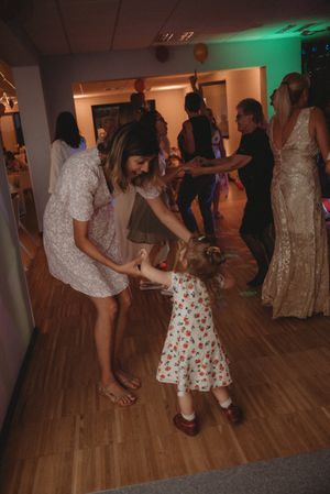 Adult and child dancing together on wooden floor at wedding reception.