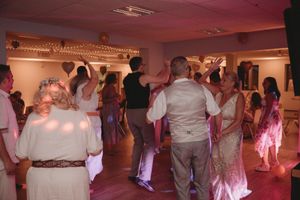 Wedding guests dancing in dimly lit reception hall with pink lighting effects.