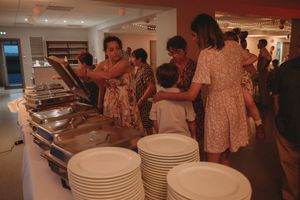 People serving themselves food at a buffet line with stacked white plates and warming trays.