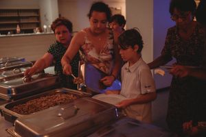 Family members serving food from warming trays at a casual buffet setup.