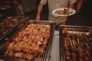 Grilled meat skewers and chicken displayed in metal catering trays.