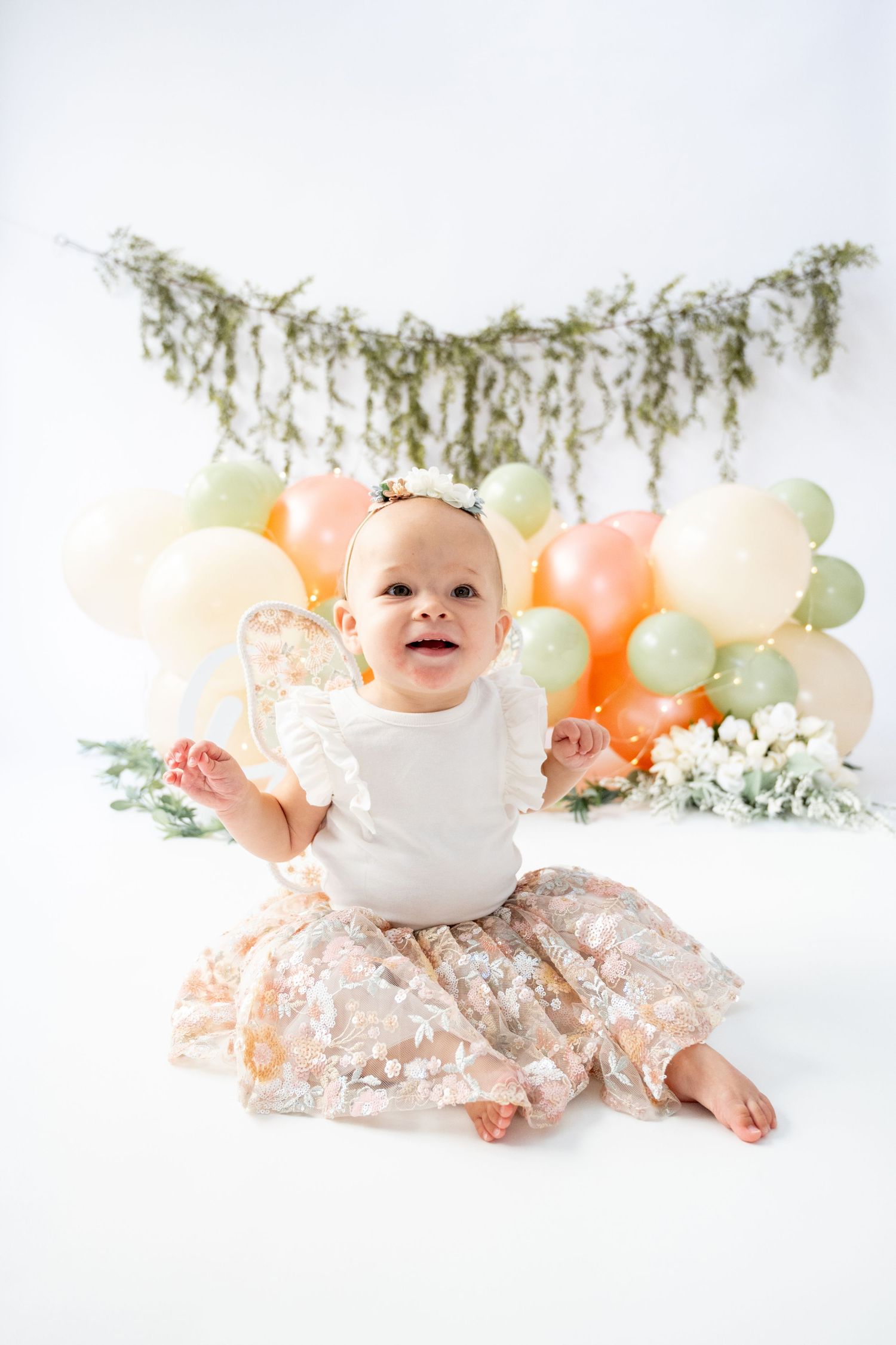 Baby photoshoot setup with peach and mint balloons and greenery garland on white background.