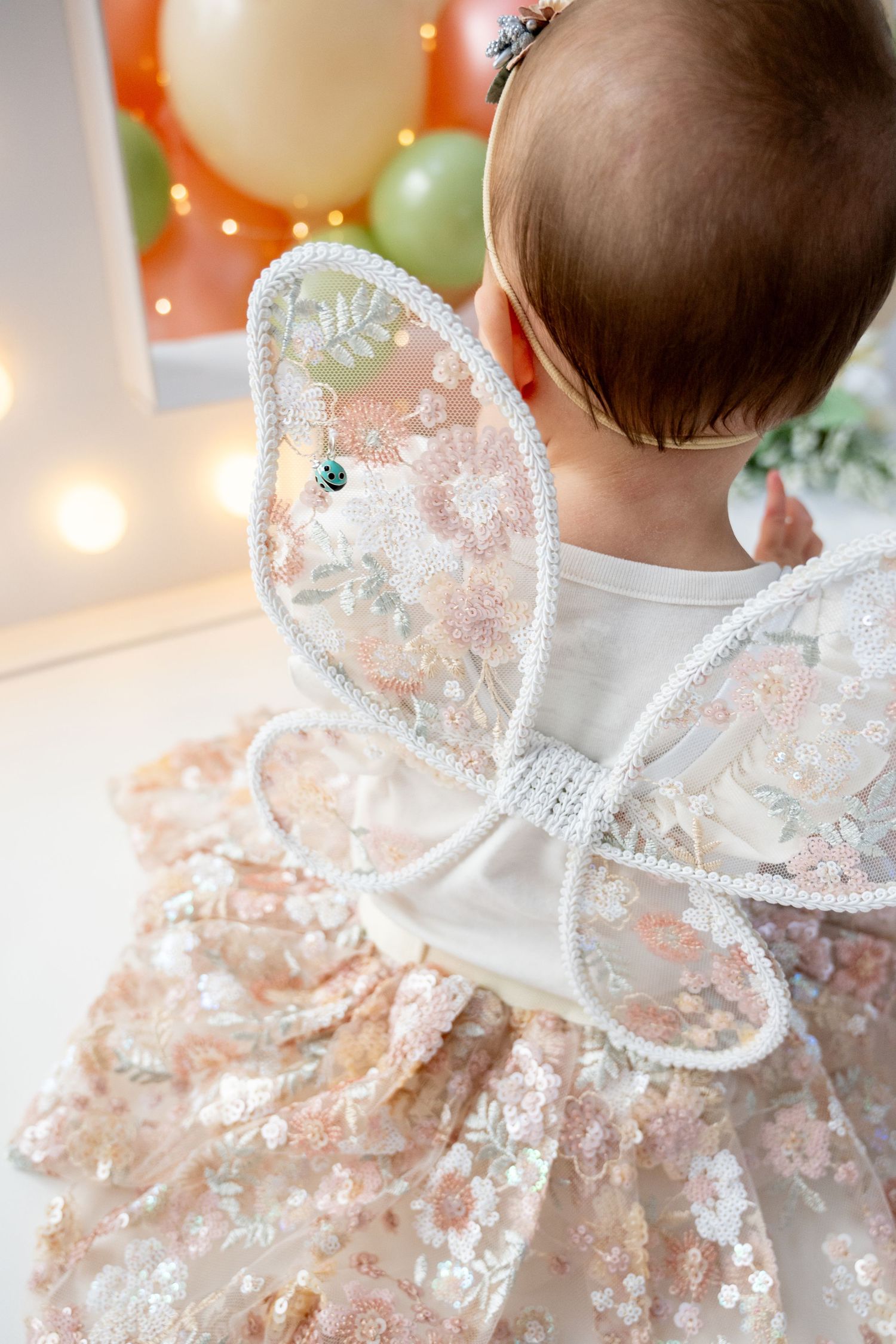 Delicate lace details on white dress with pastel balloons in background.