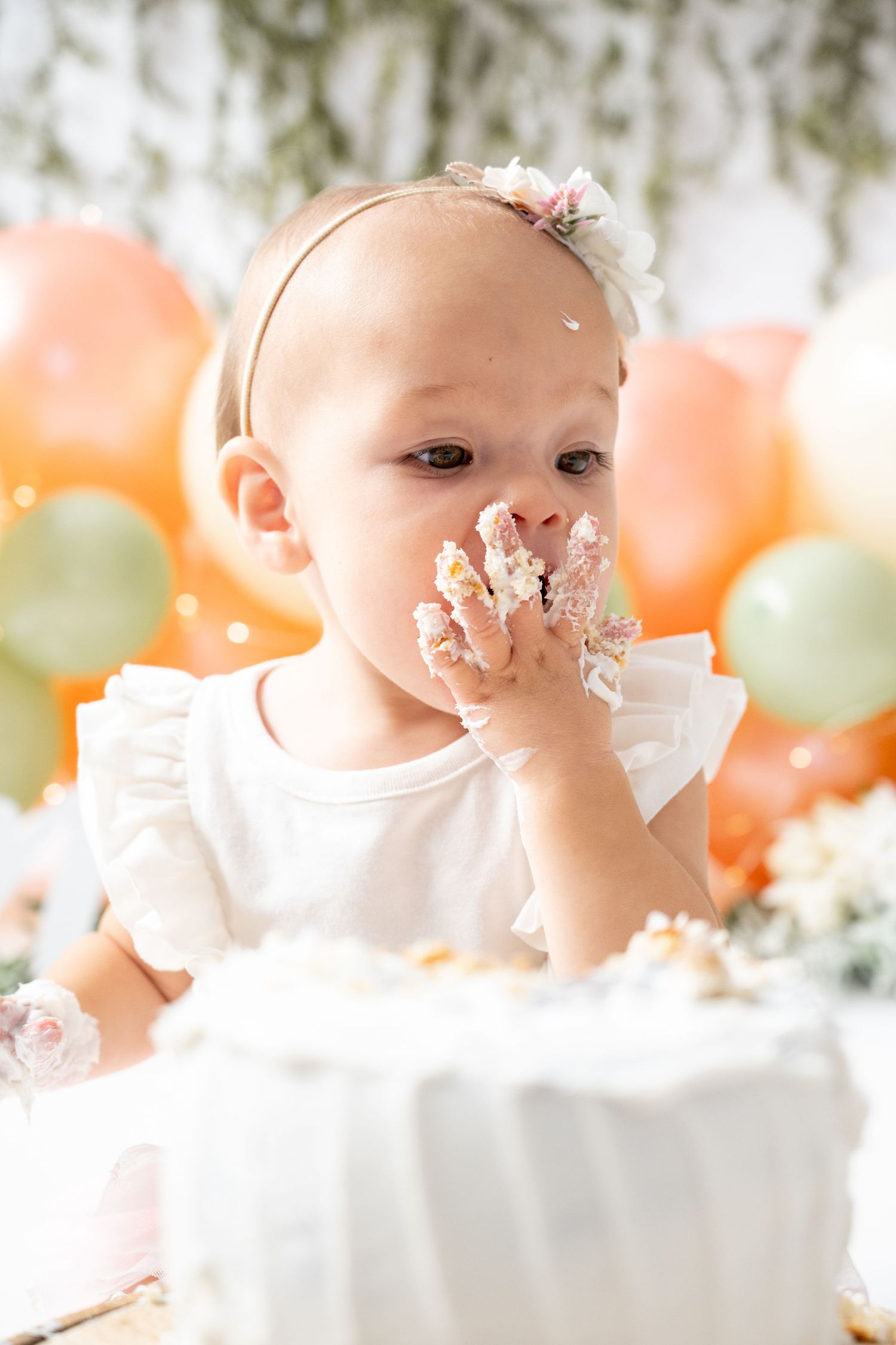Cake smash photo session with peach and mint balloons decorating the background.