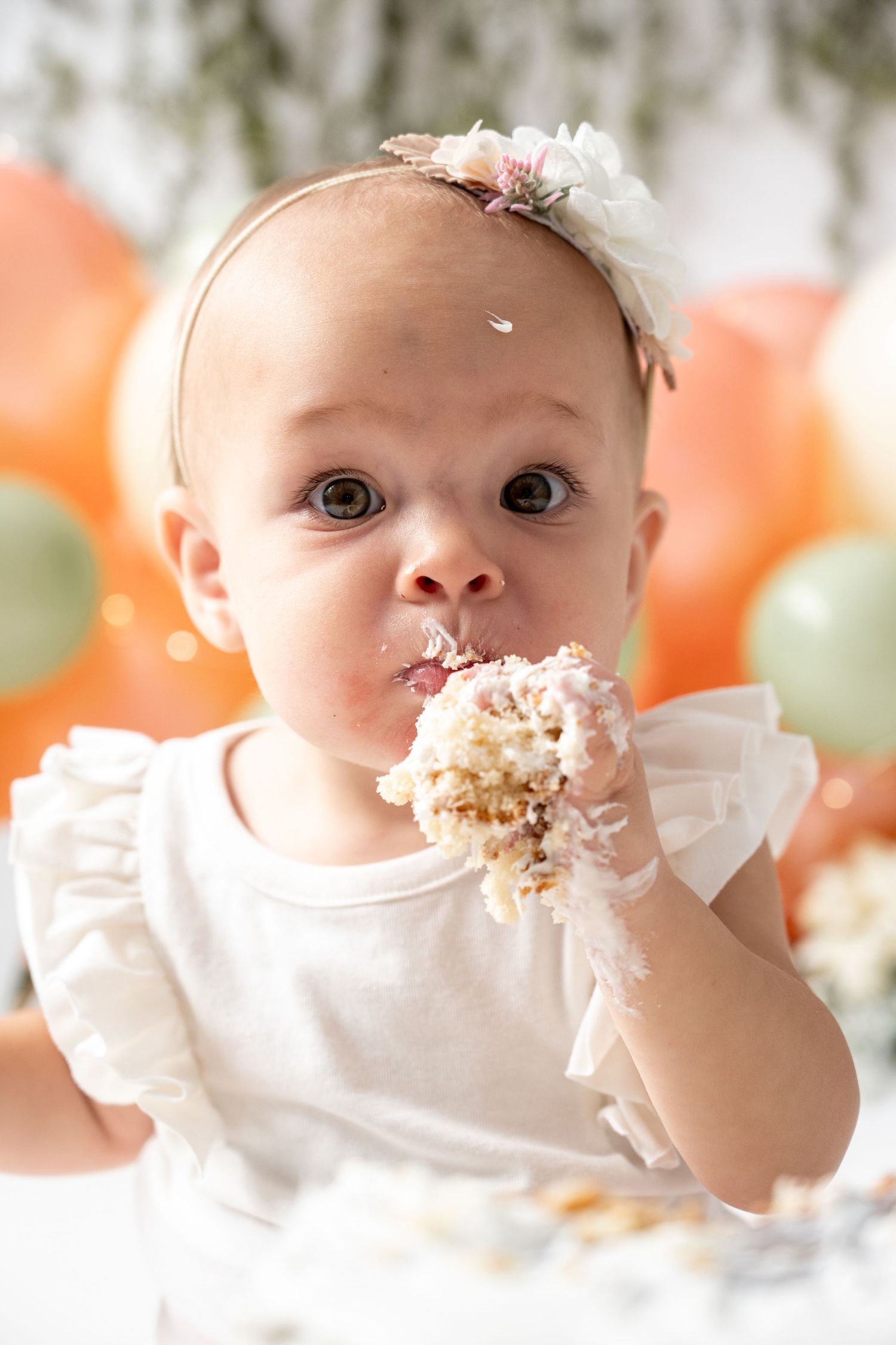 First birthday cake smash session with white cake and festive balloon backdrop.