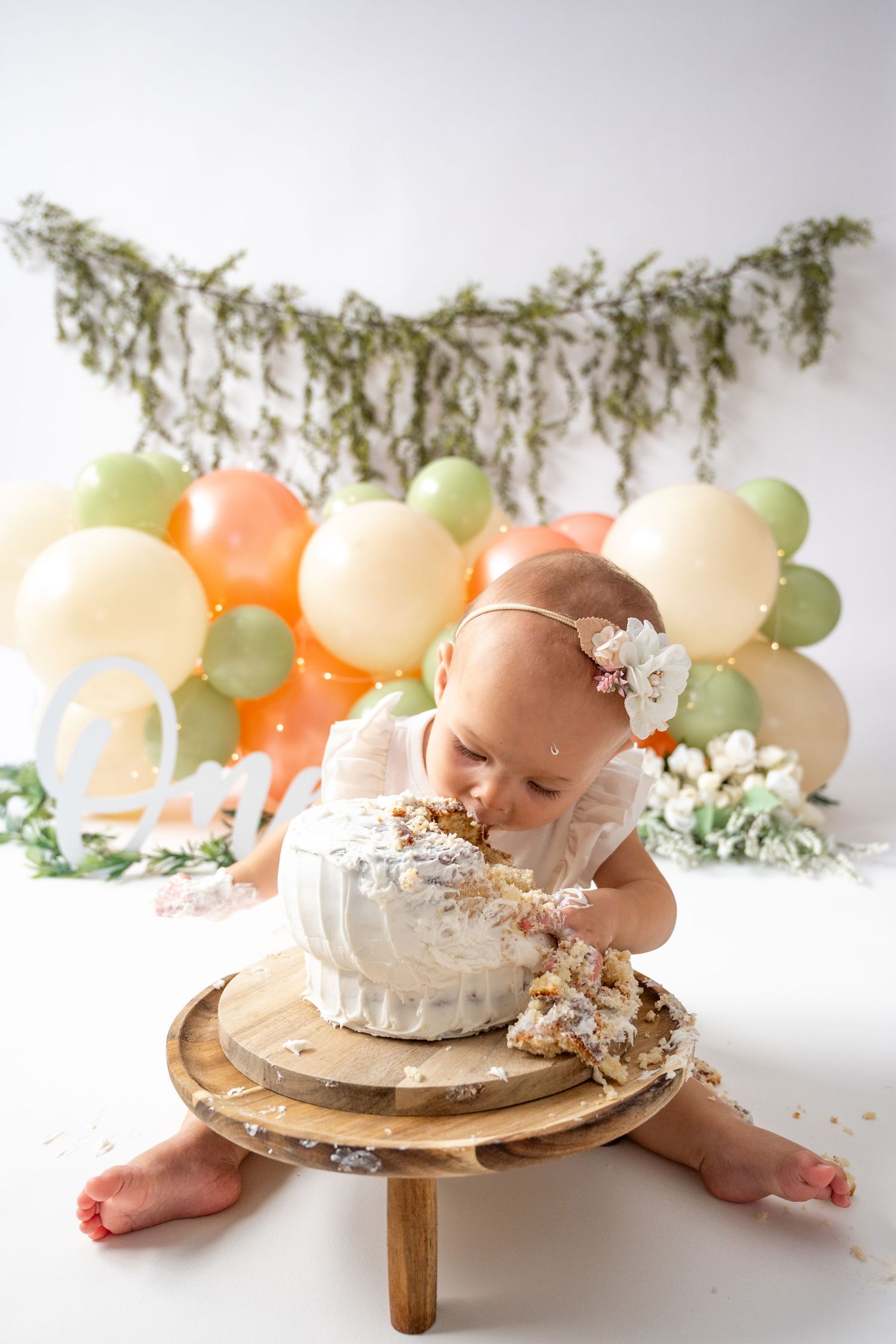 Cake smash photography setup with wooden stand and pastel balloon garland.