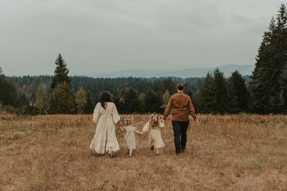 mom dad two little girls and one baby girls in an open field with rolling hills in the background smiling and playing