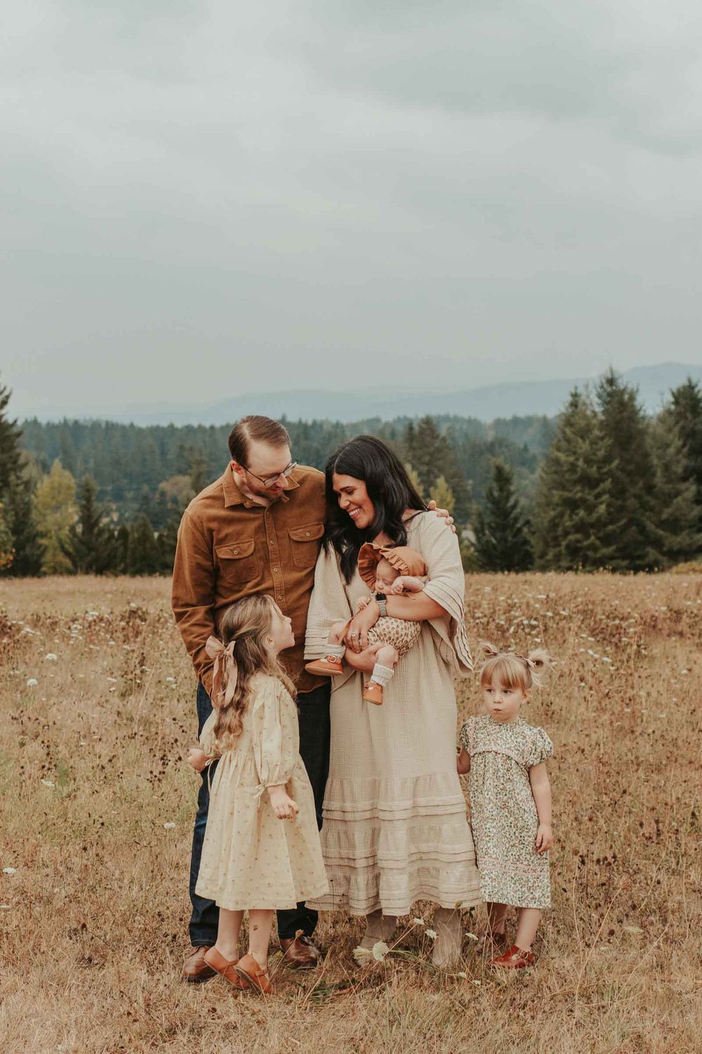 mom dad two little girls and one baby girls in an open field with rolling hills in the background smiling at each other