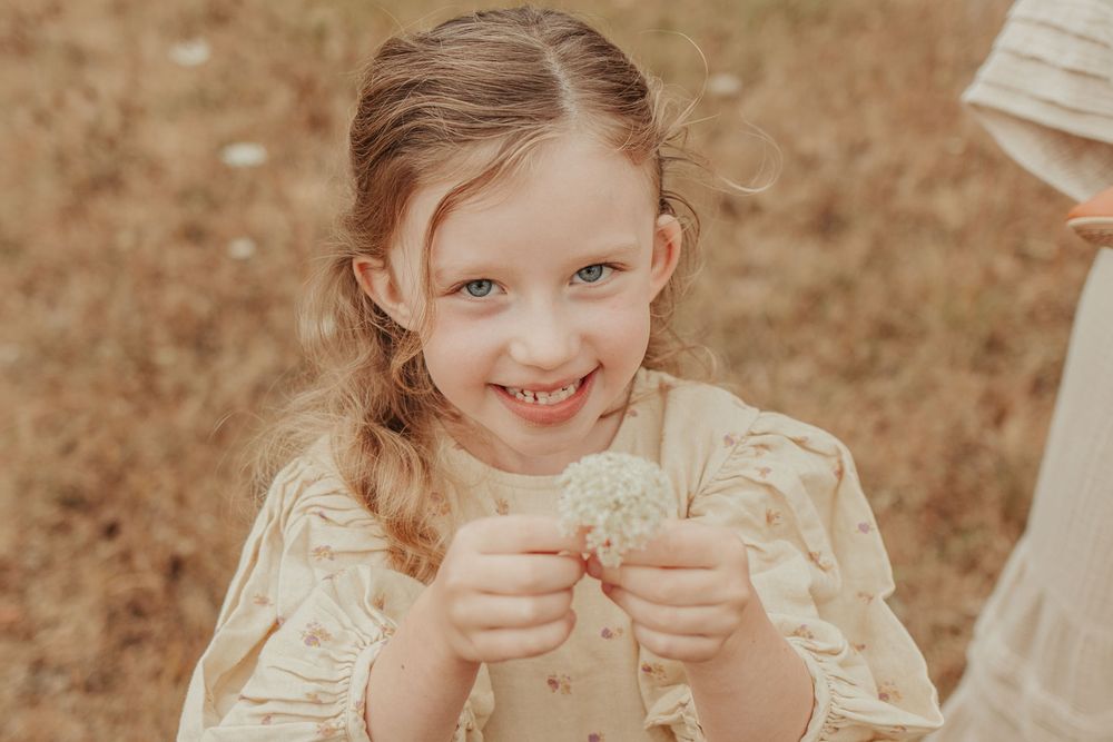 blonde little girl in an open field holding up a dandilion flower