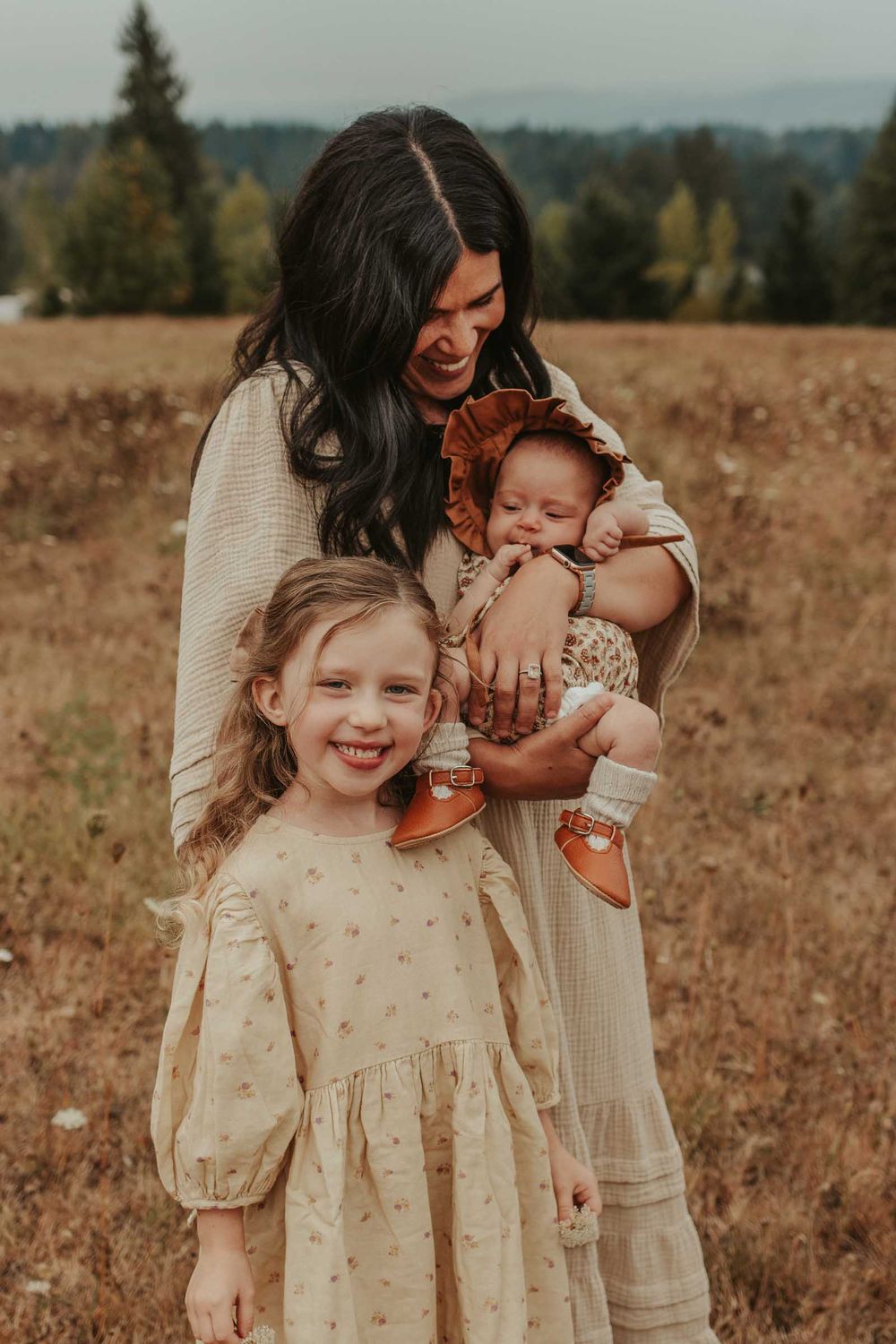 mother holding a newborn baby in an open flower field with big sister