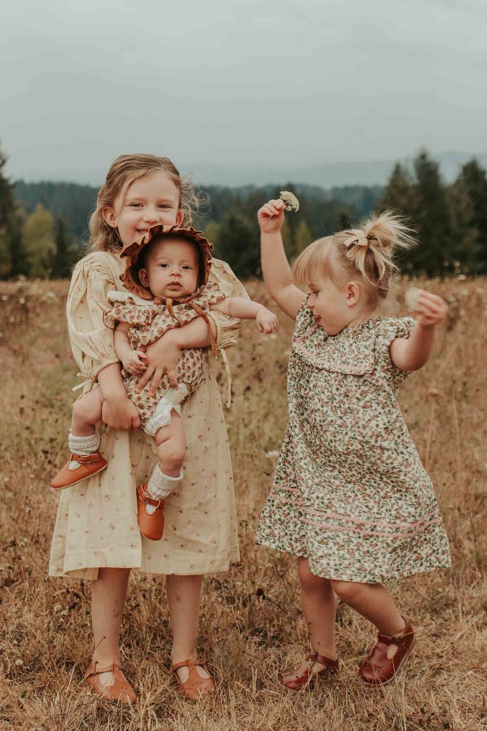 two little girls holding their baby sister in a flower field
