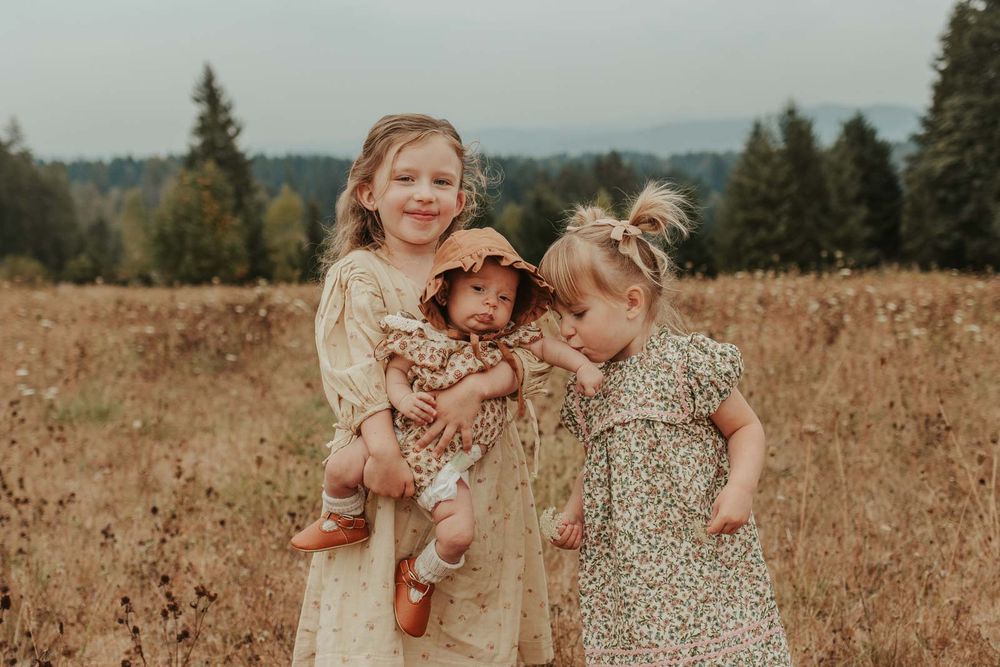two little girls holding their baby sister in a flower field