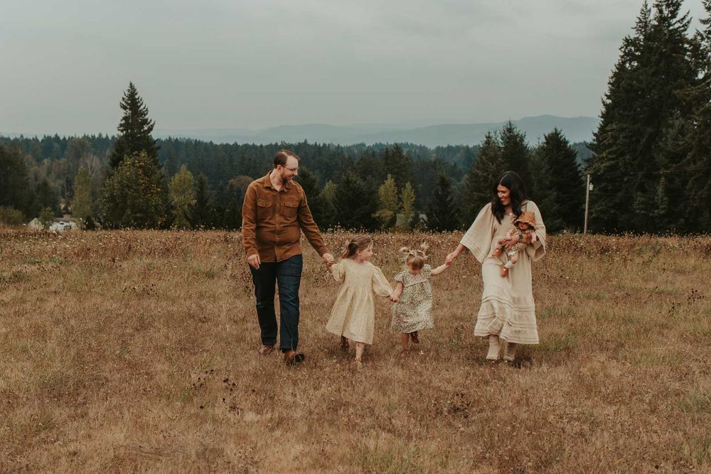 mom dad two little girls and one baby girls in an open field with rolling hills in the background walking holding hands