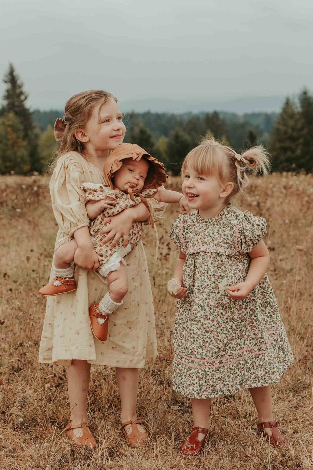 two little girls holding their baby sister in a flower field