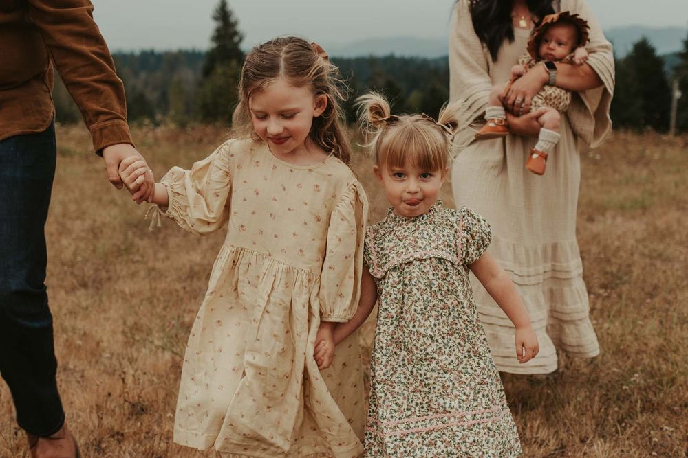 mom dad two little girls and one baby girls in an open field with rolling hills in the background smiling and playing