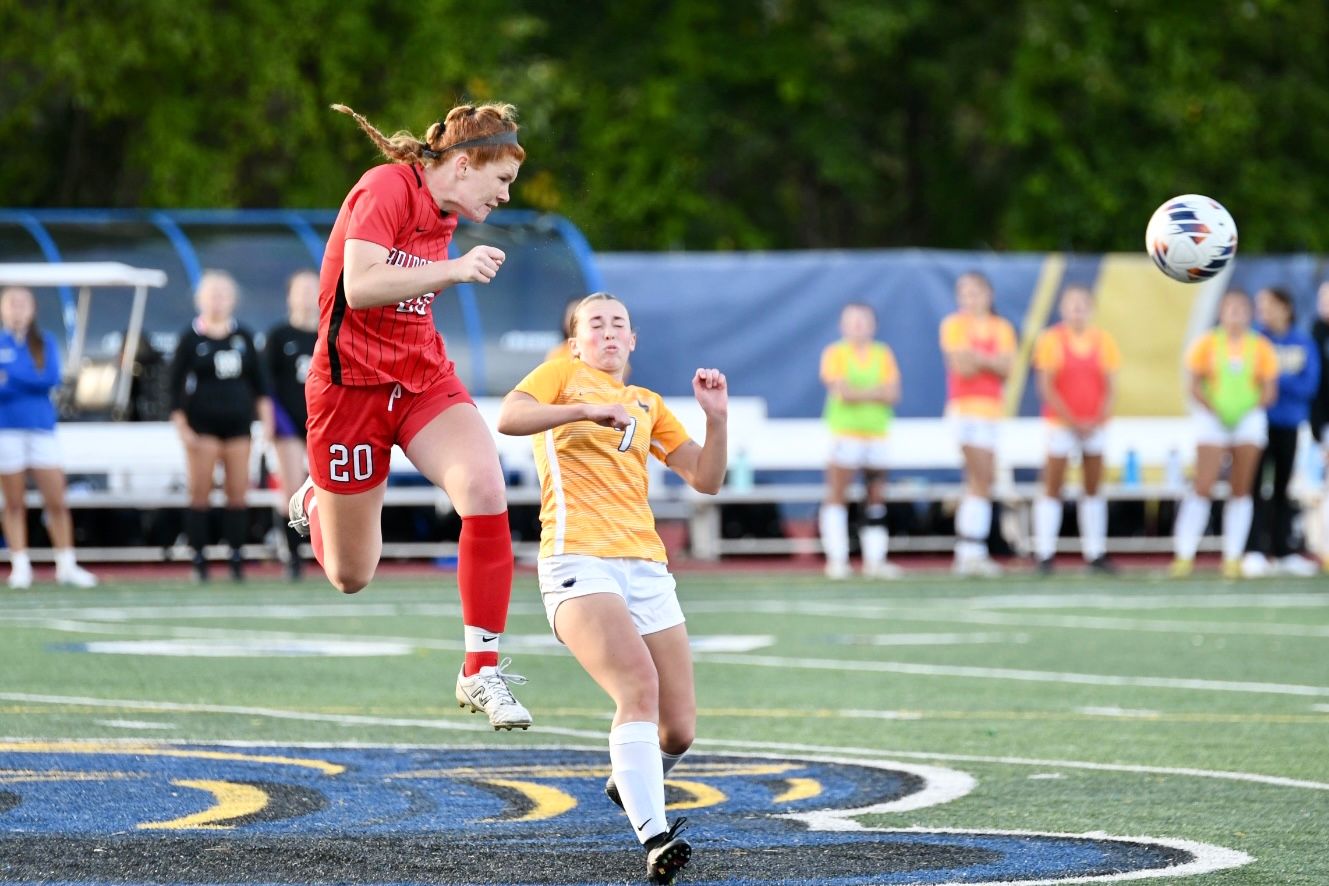 Players competing for a header during a soccer match with spectators in the background.