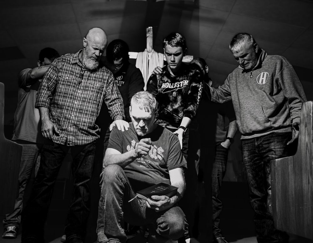 A black and white photo shows a group of people huddled together around someone sitting in a chair on stage.