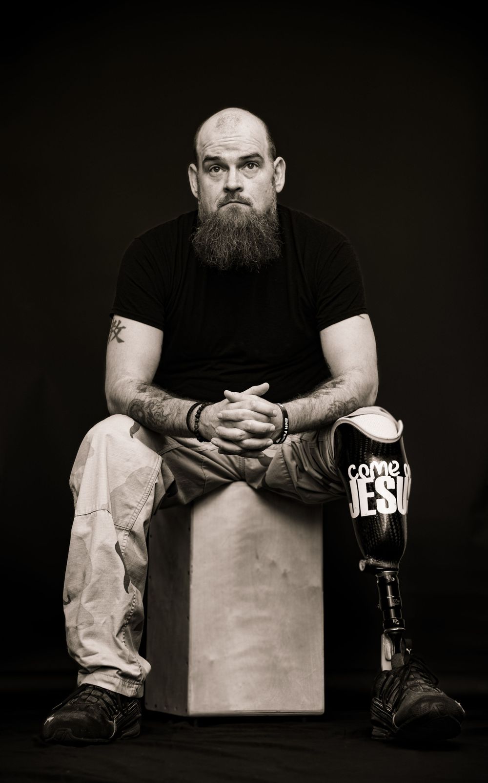 Black and white portrait of a person sitting on a cube wearing casual attire with a prosthetic leg.
