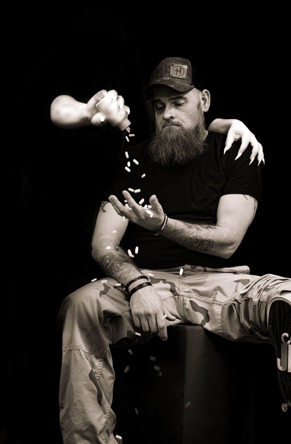 Black and white artistic photo of someone in a cap pouring something into their hand while sitting.