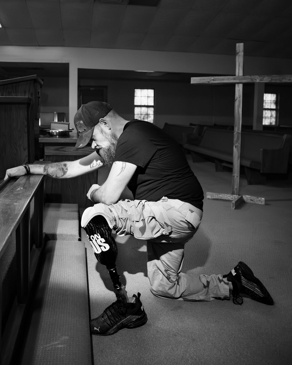Person kneeling in prayer at church pew with wooden cross visible in the background.