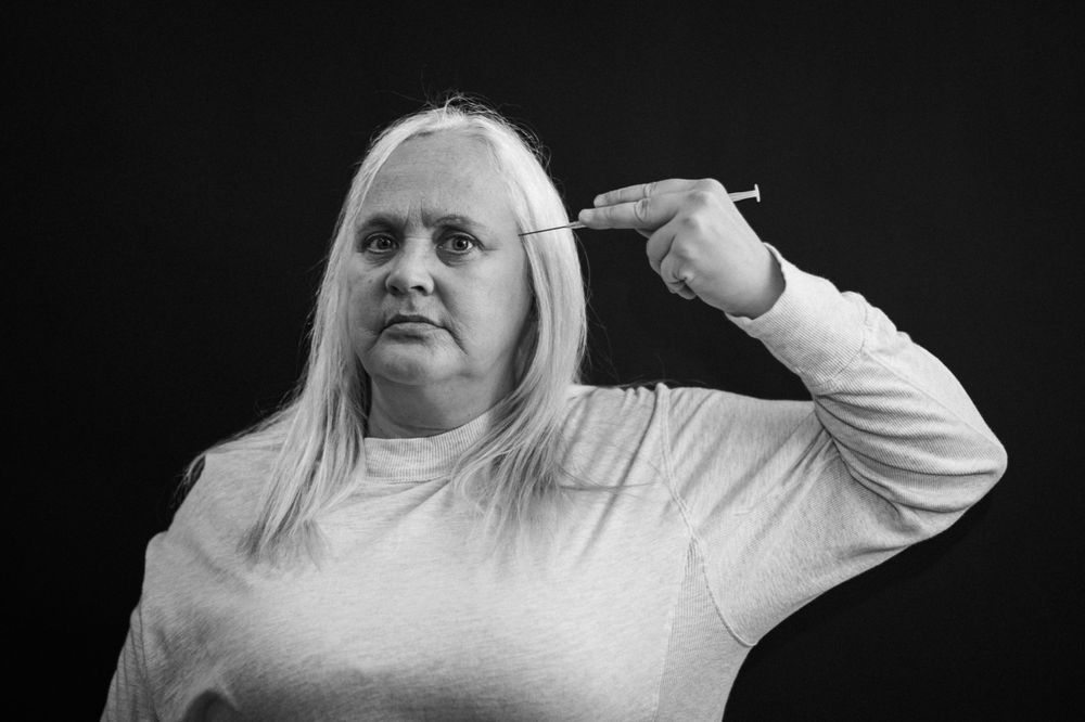 Black and white portrait of someone gesturing with fingers pointed at their head in a contemplative expression.