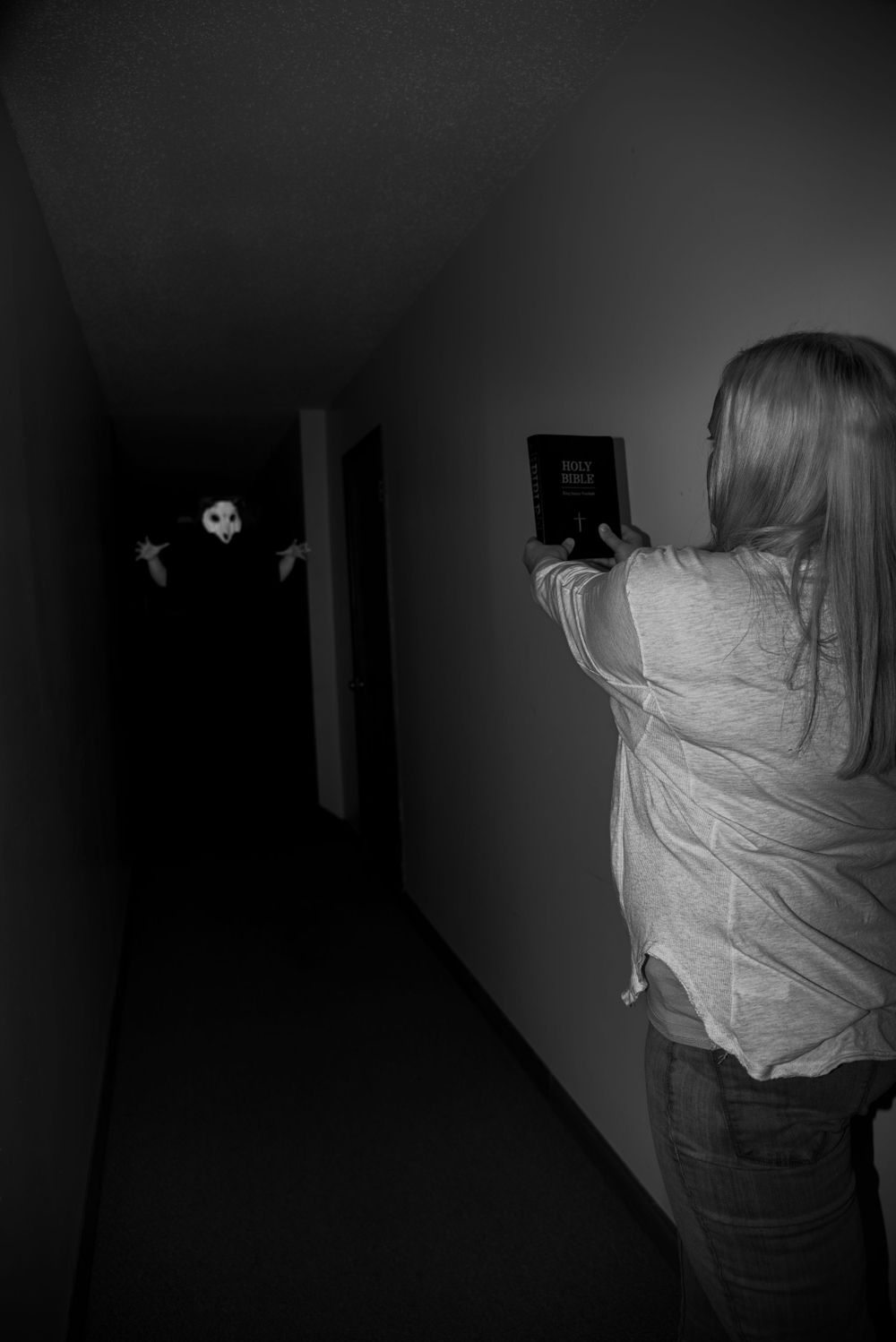 A spooky black and white photo in a dark hallway showing someone holding a camera in front of what appears to be a ghost.