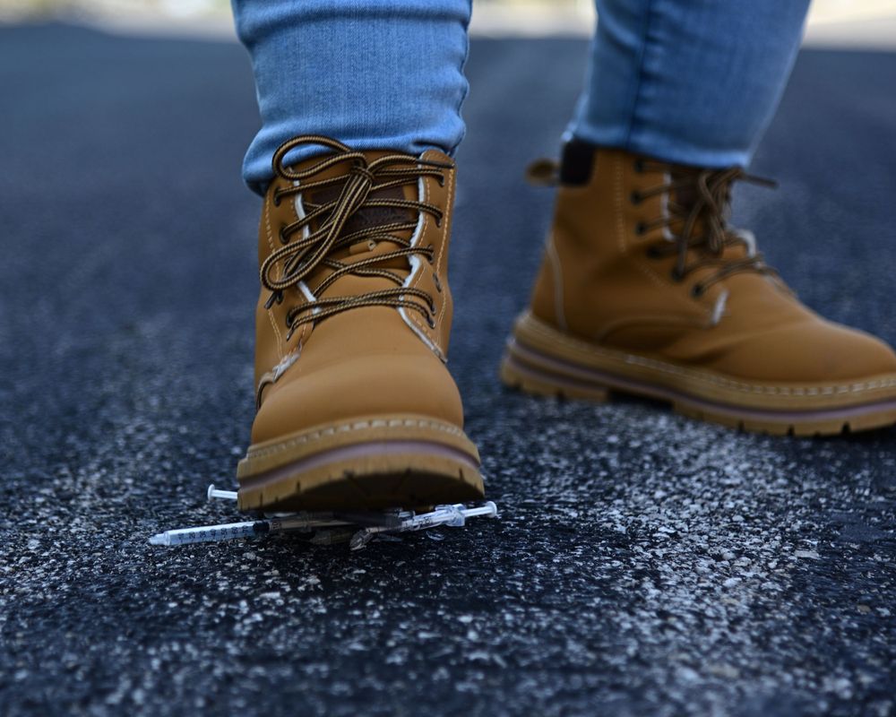 Close up of tan leather work boots with blue jeans on a dark asphalt surface.