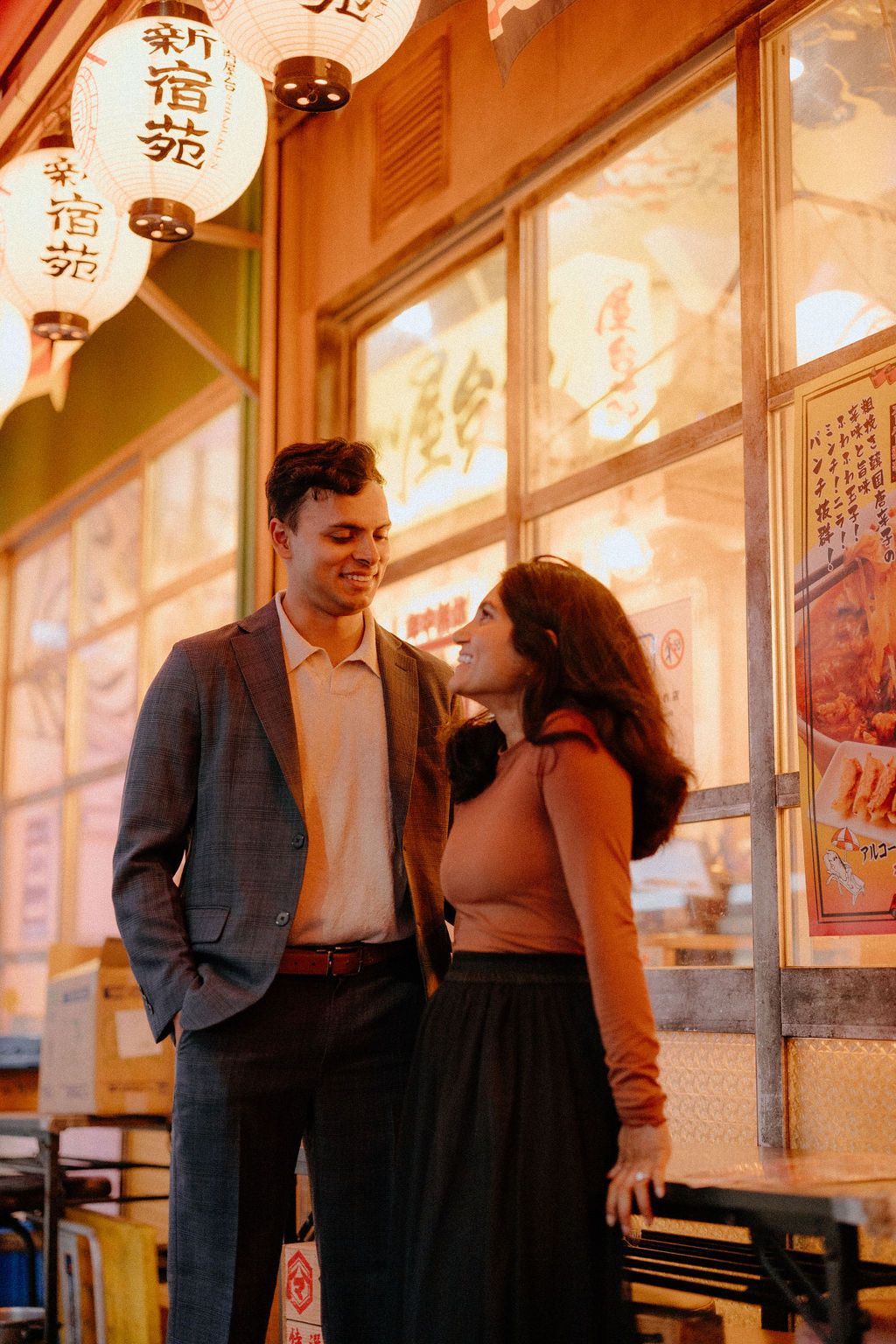 Couple shares romantic moment under glowing Japanese lanterns and storefront signs.