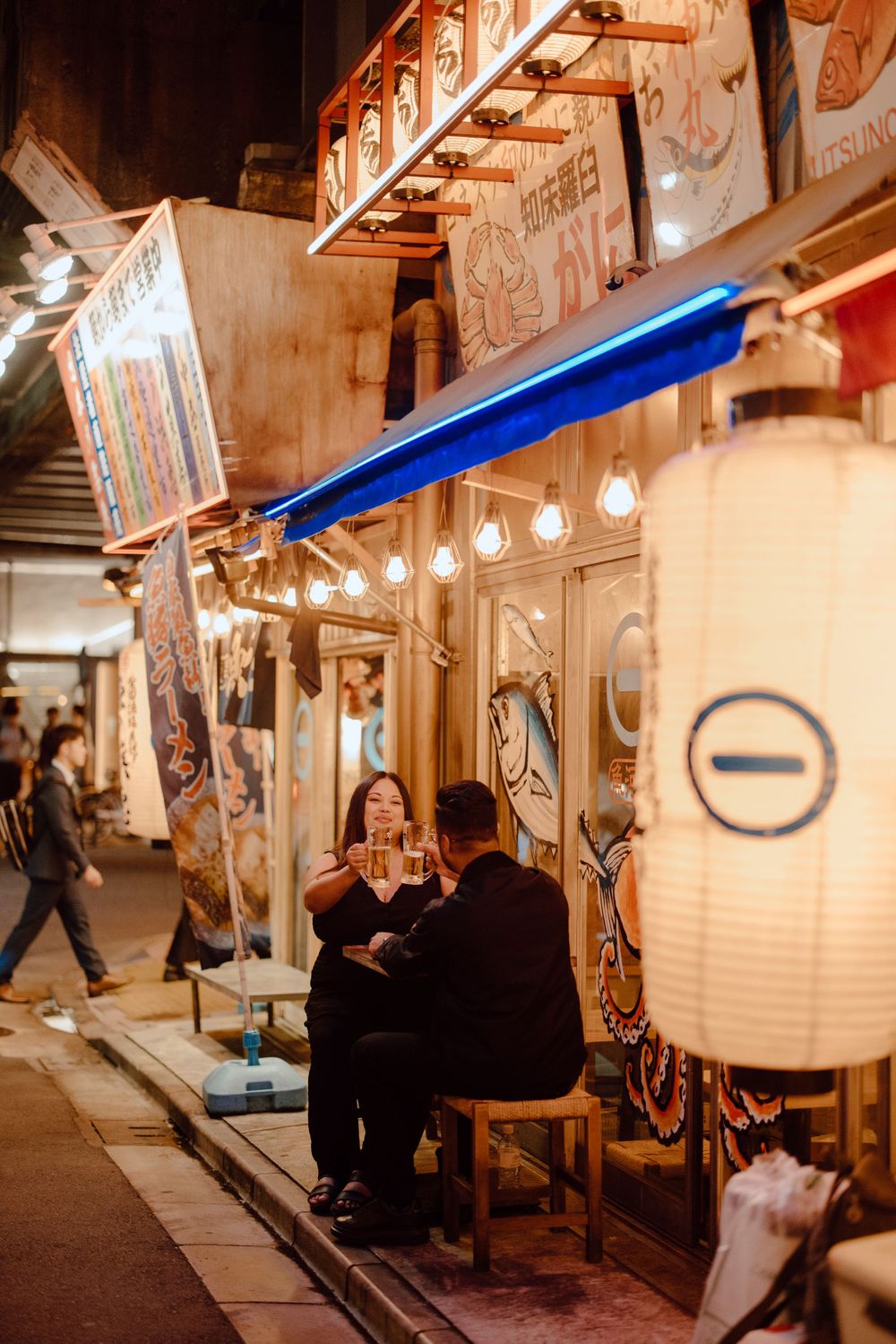 Cozy nighttime scene at Japanese restaurant with traditional paper lanterns illuminating outdoor seating area along narrow street.