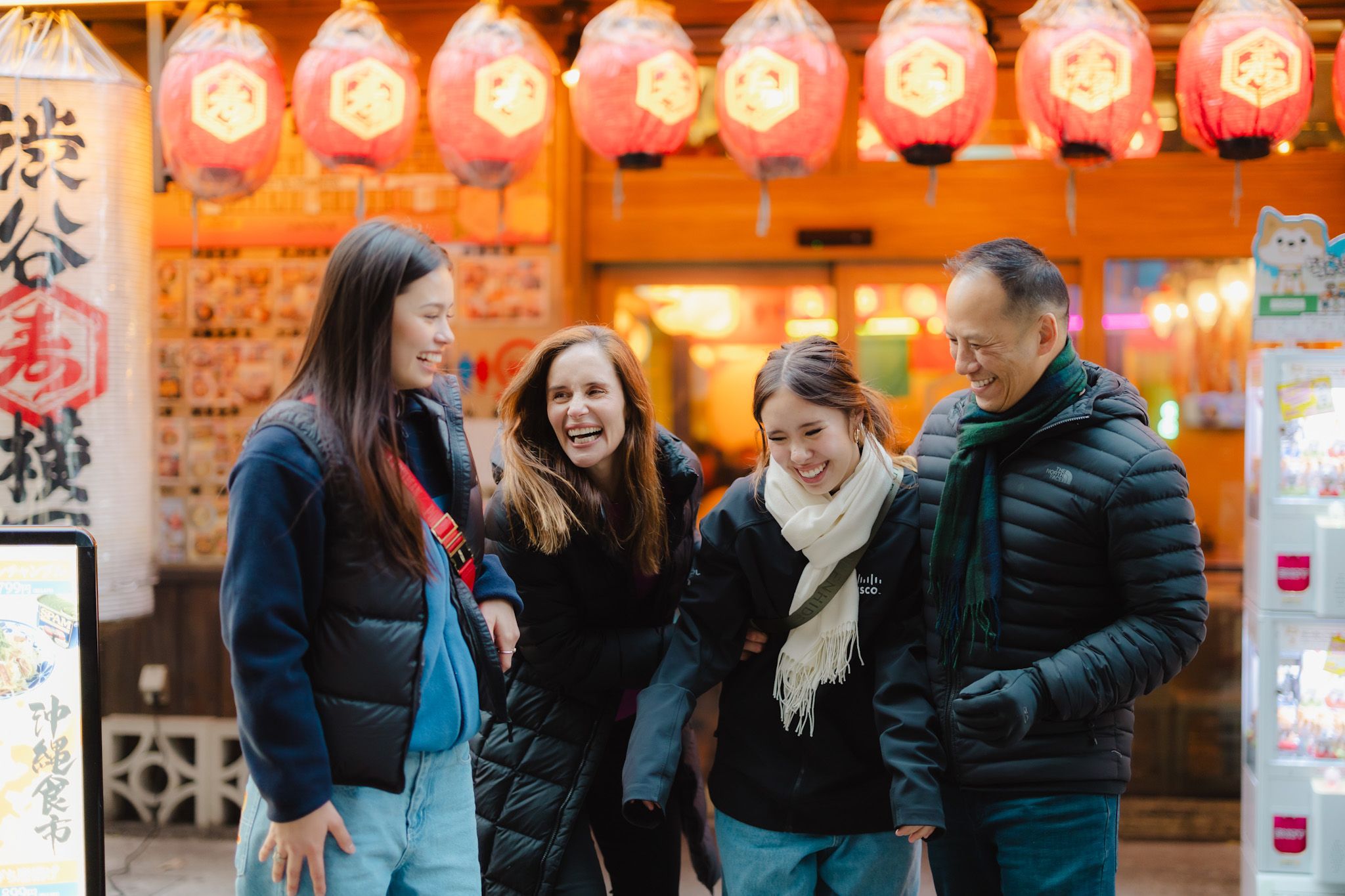 A group of people share a joyful moment under glowing lanterns outside an Asian restaurant at night.