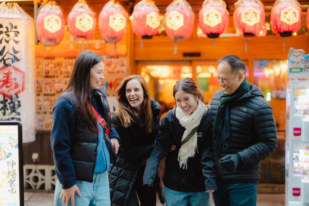 A group of people share a joyful moment under glowing lanterns outside an Asian restaurant at night.