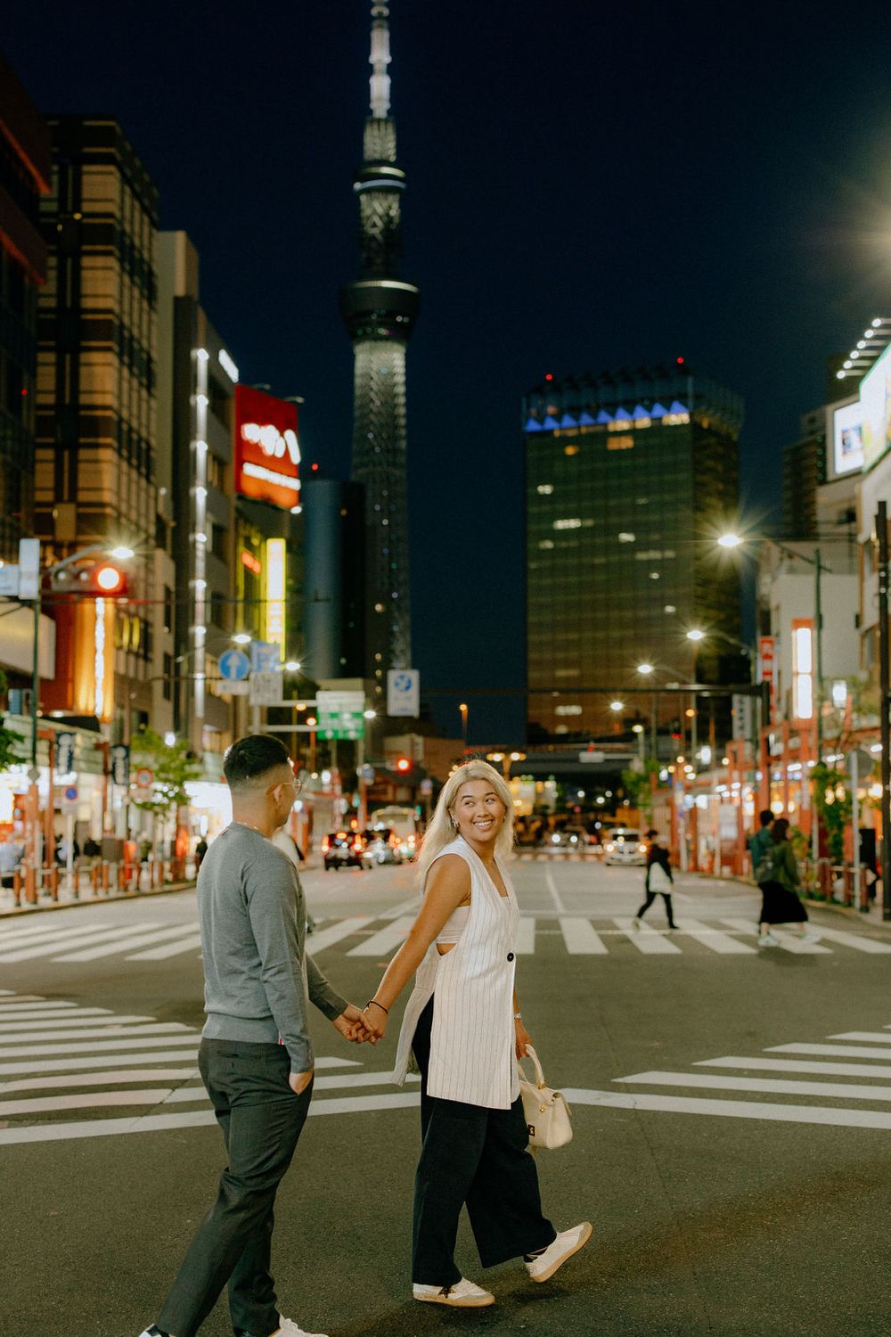 Couple crossing street at night with Tokyo Skytree illuminated in background.