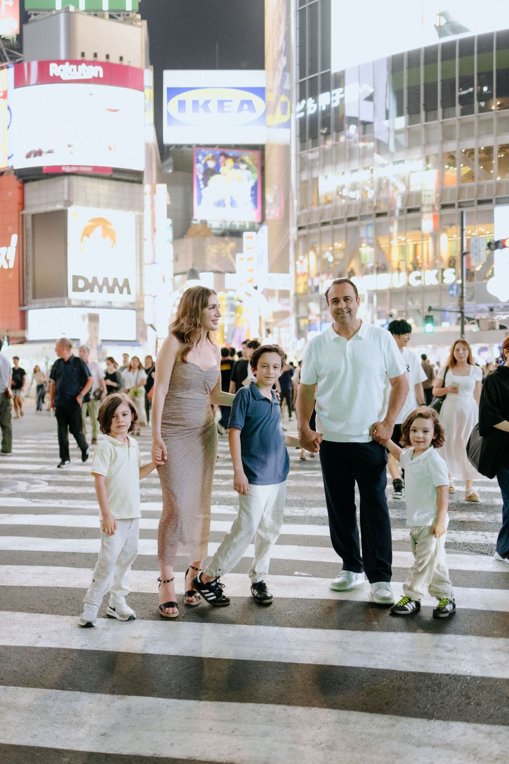 Group of people crossing the iconic Shibuya Crossing in Tokyo at night with bright commercial signs in background.