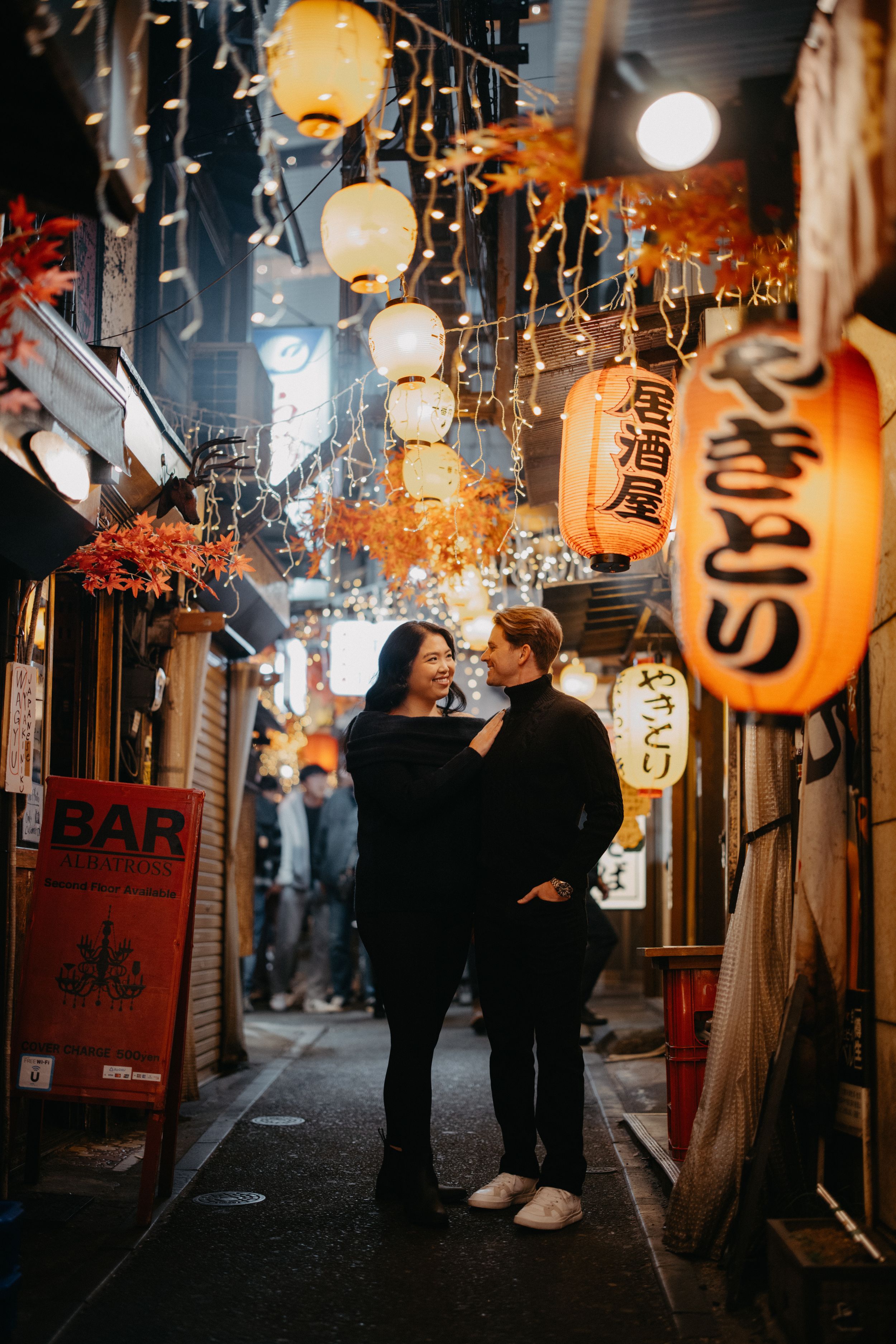 A romantic evening scene in a narrow Japanese alley with glowing lanterns and illuminated signage creating a cozy atmosphere.