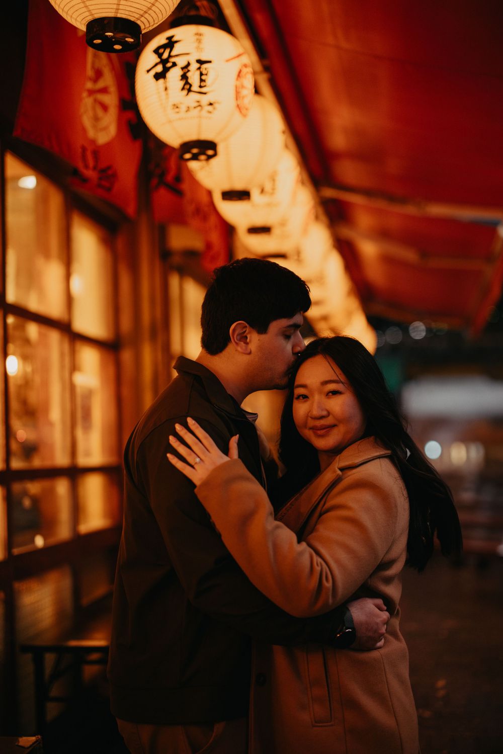 A romantic couple embraces under warm glowing Asian lanterns on a cozy evening street.