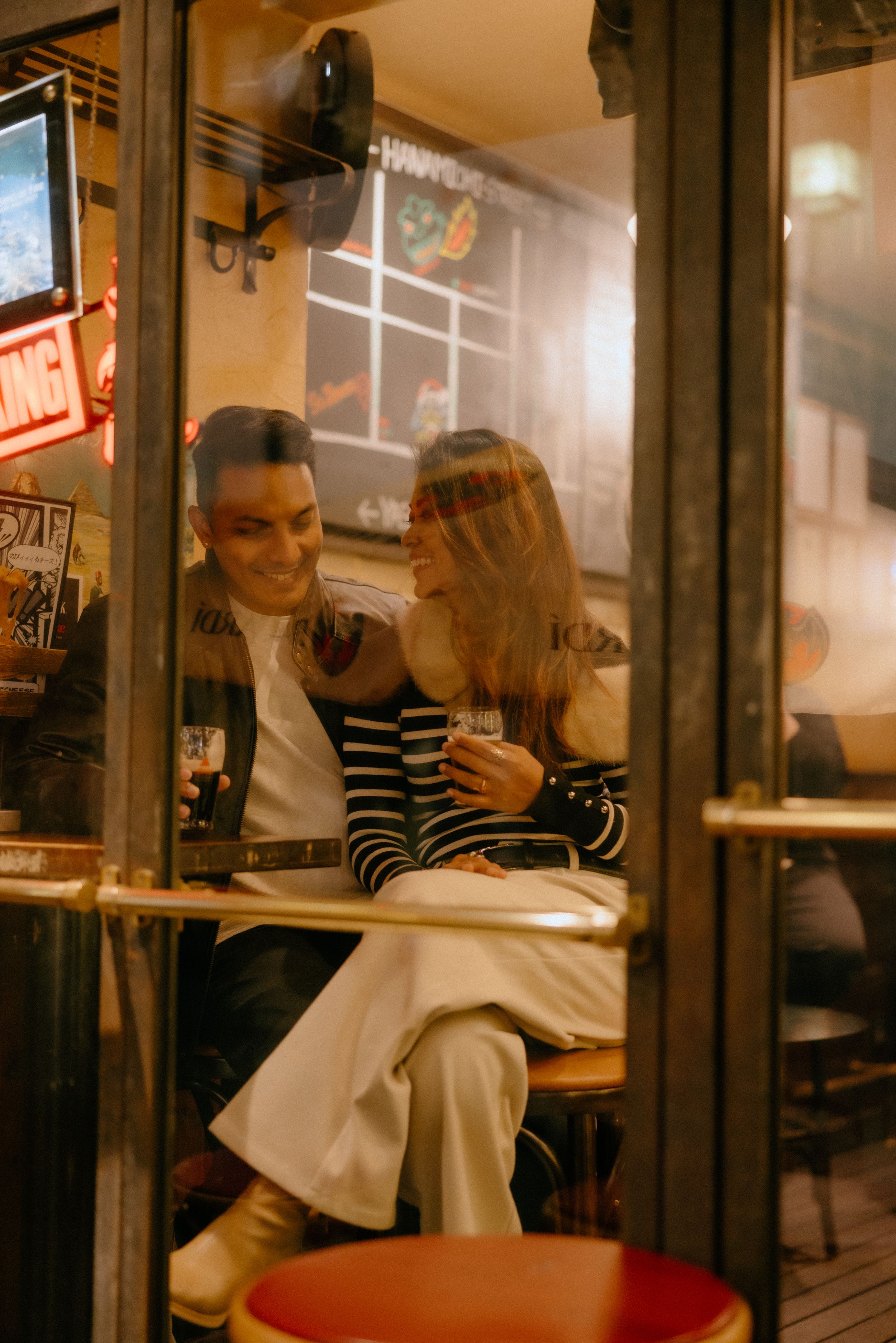 A couple sits intimately at a cozy cafe table by the window, captured in warm vintage tones on a night out.