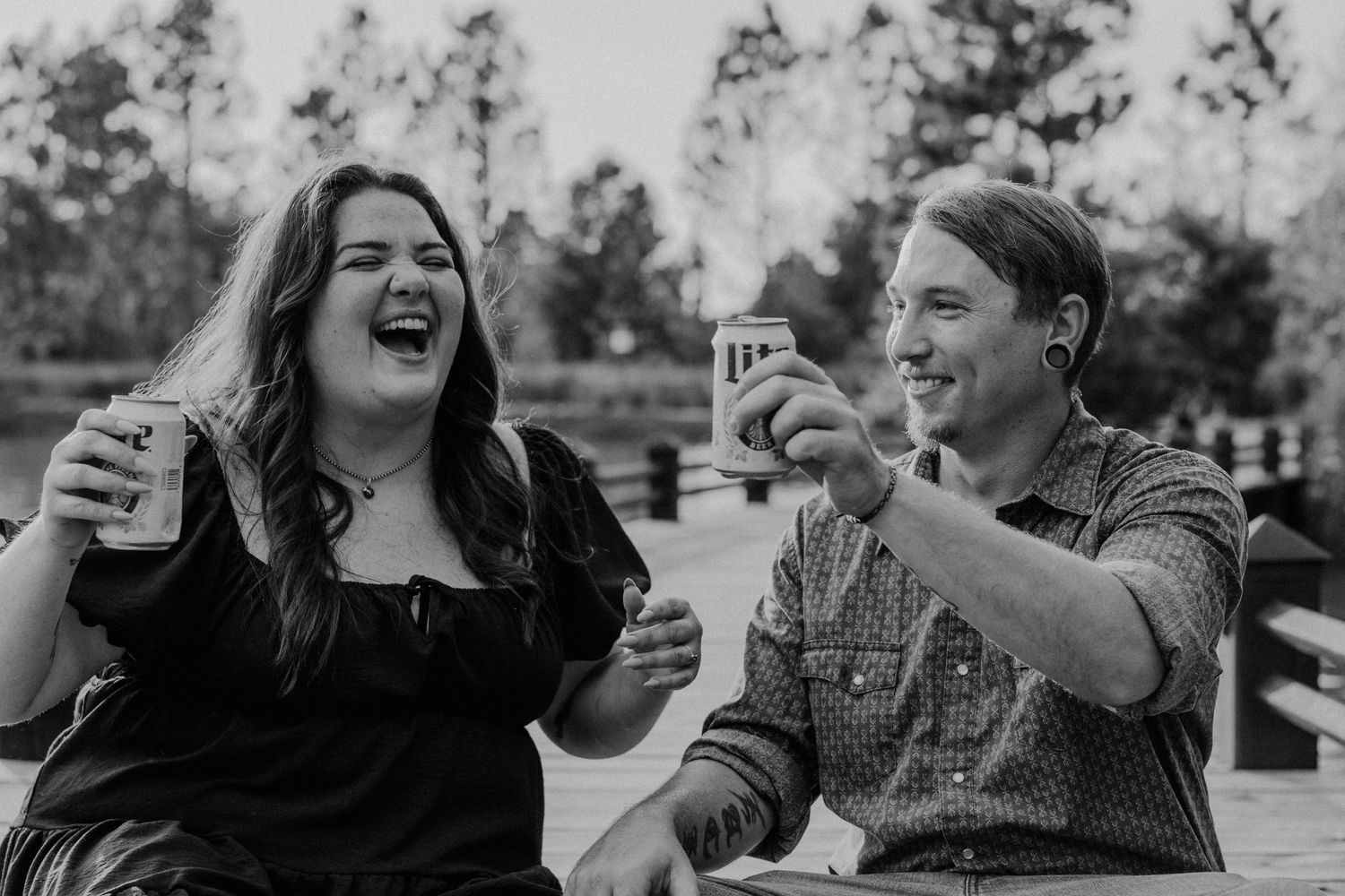 Two people sharing drinks and laughing together outdoors in a candid black and white moment.