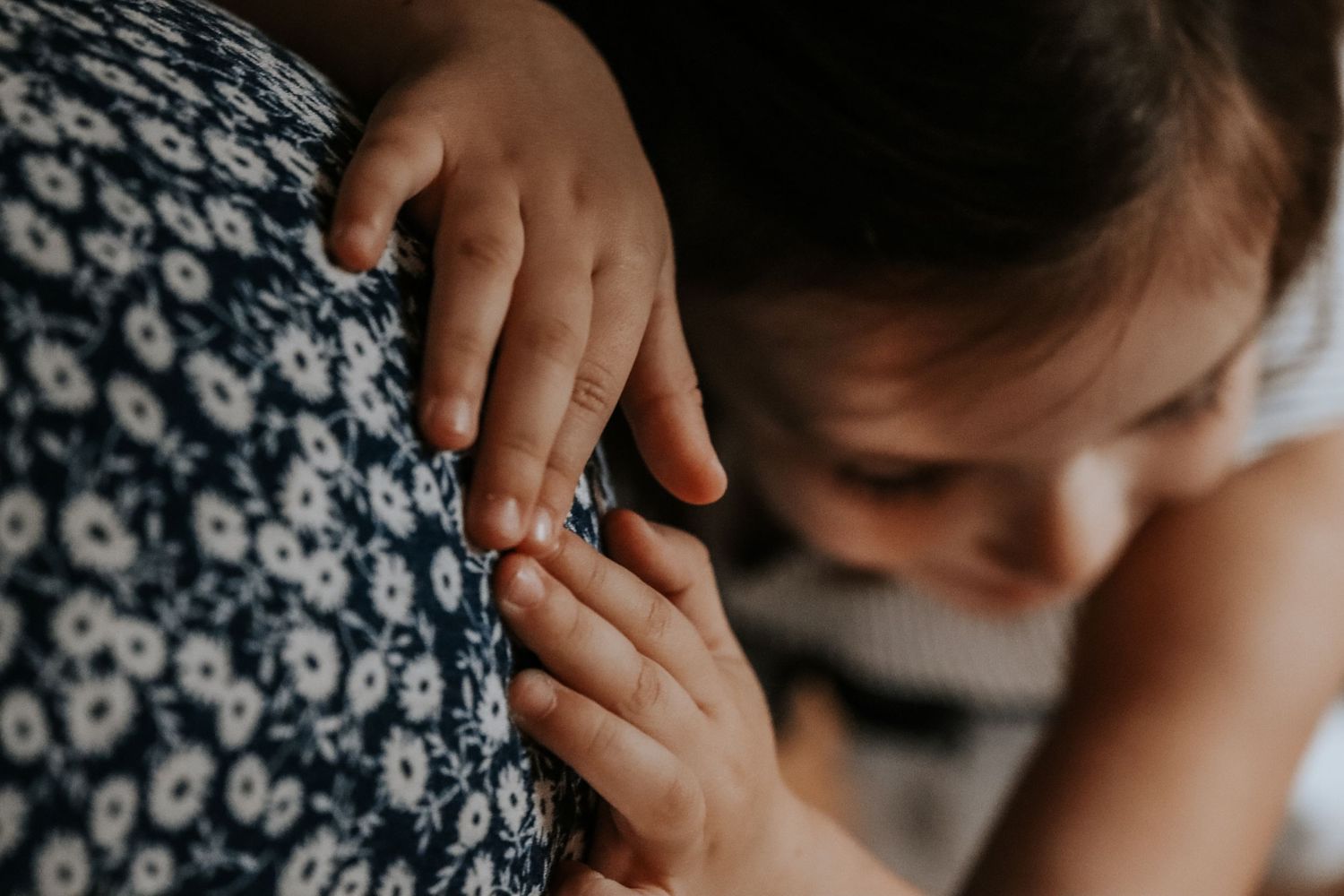 Close-up of a young child's hands gently touching a floral blue and white dress, capturing a tender moment.