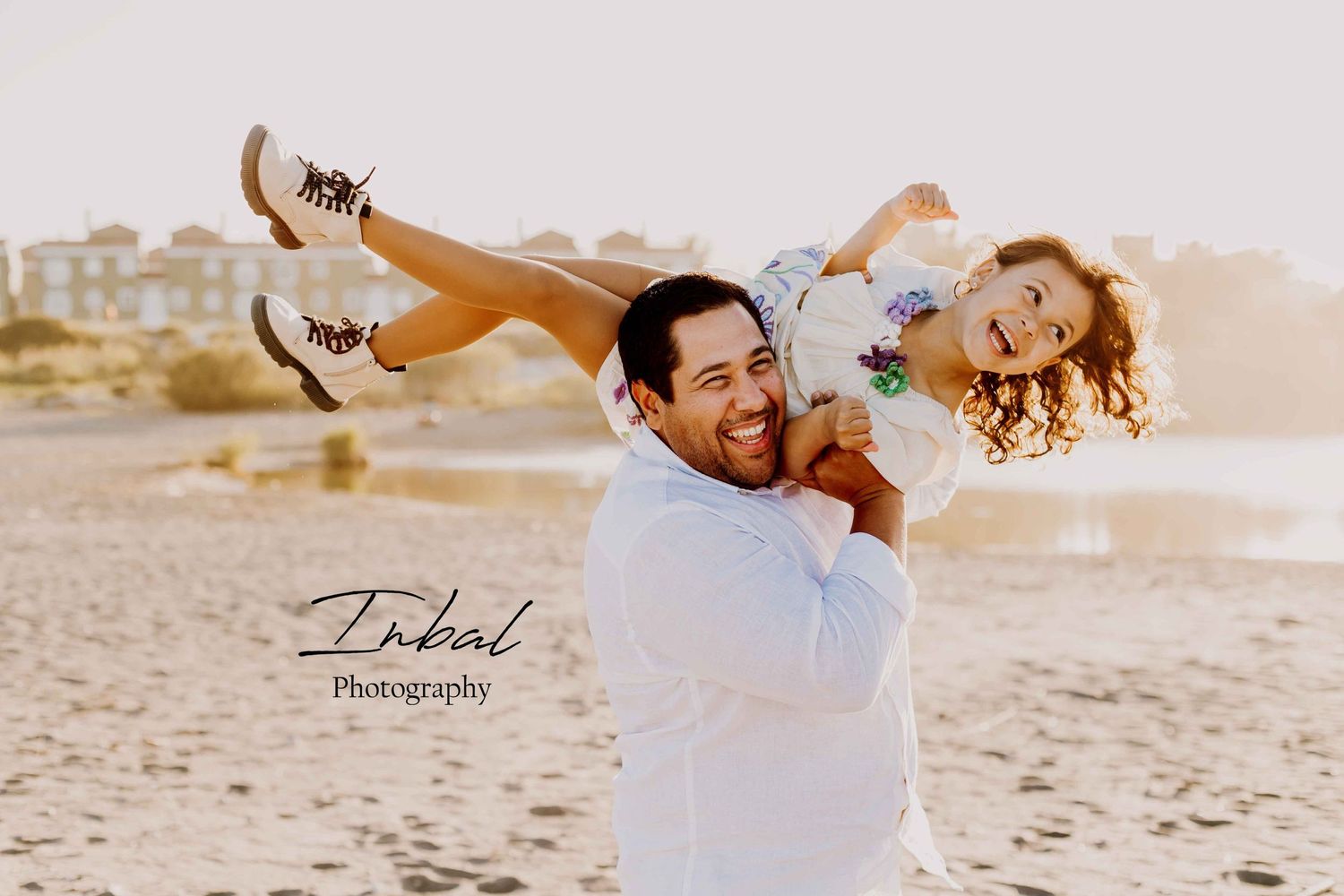 A father lifts his daughter onto his shoulders on the beach having fun during family photo session in the nature.