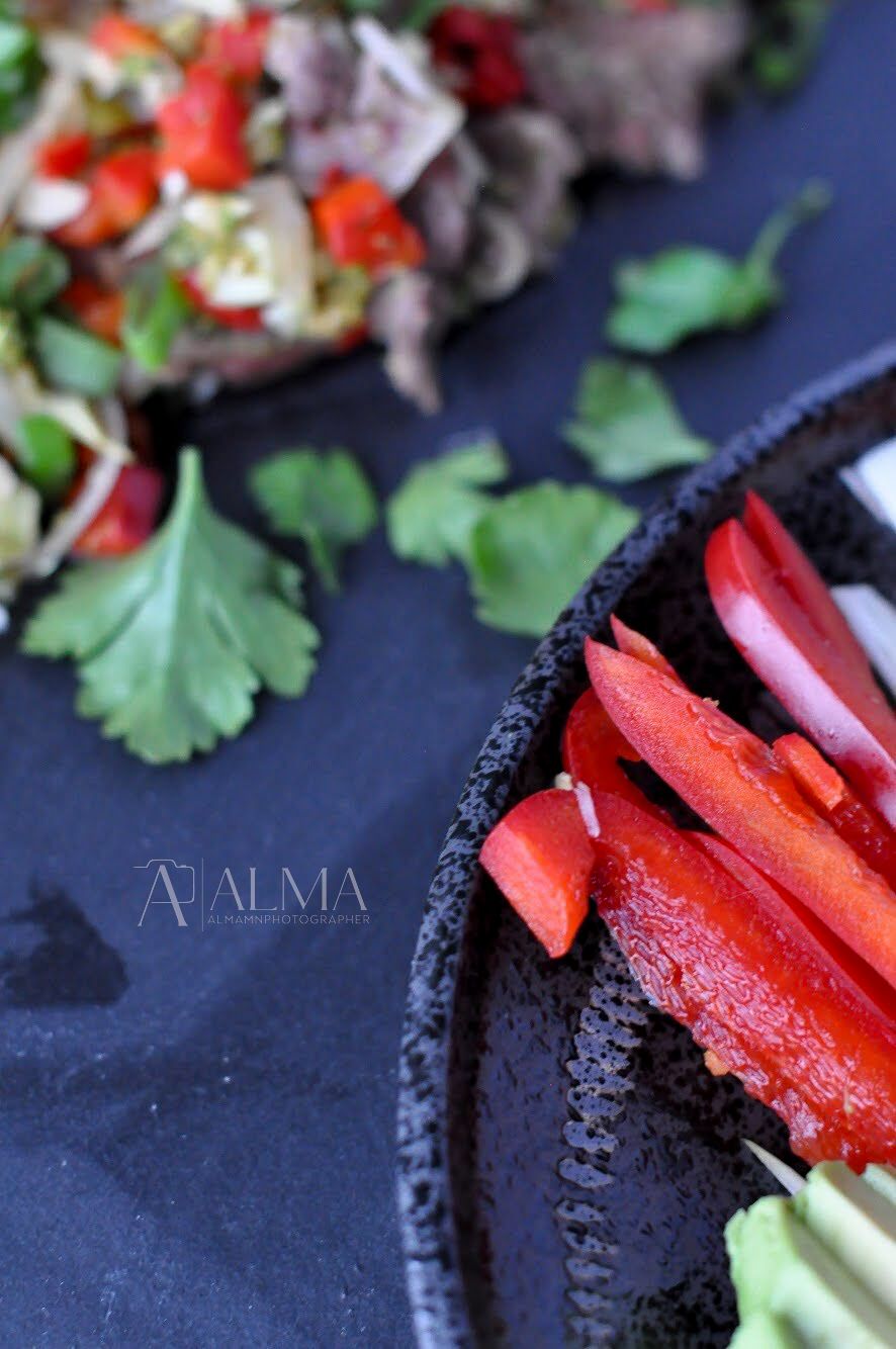 Fresh red bell peppers and herbs arranged on a black slate plate.