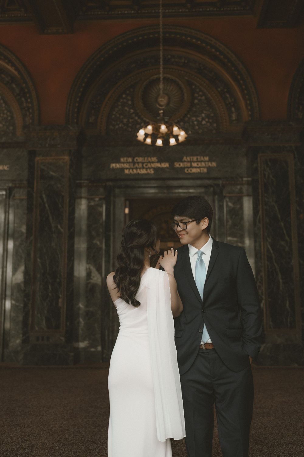 Couple in wedding attire sharing a romantic moment inside an ornate marble building with arched decor.